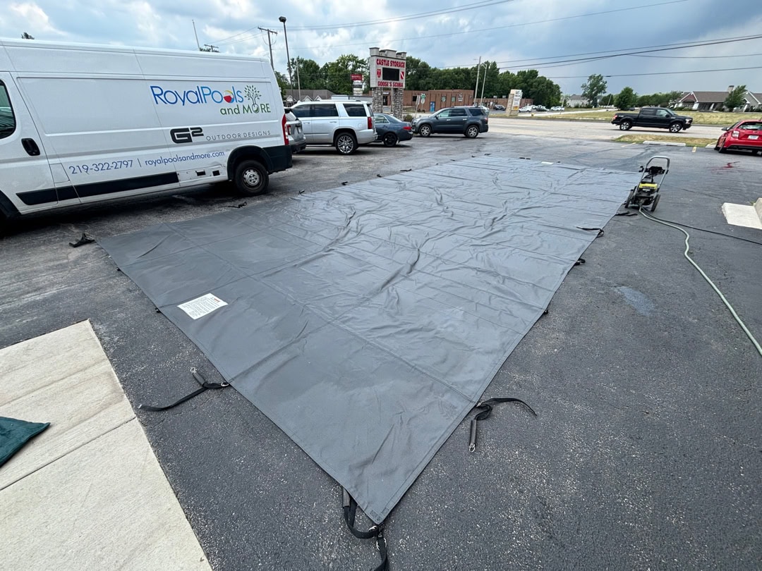 A recently cleaned solid winter cover laying open in a parking lot with a Royal Pools G2 Landscaping van right next to the cover.