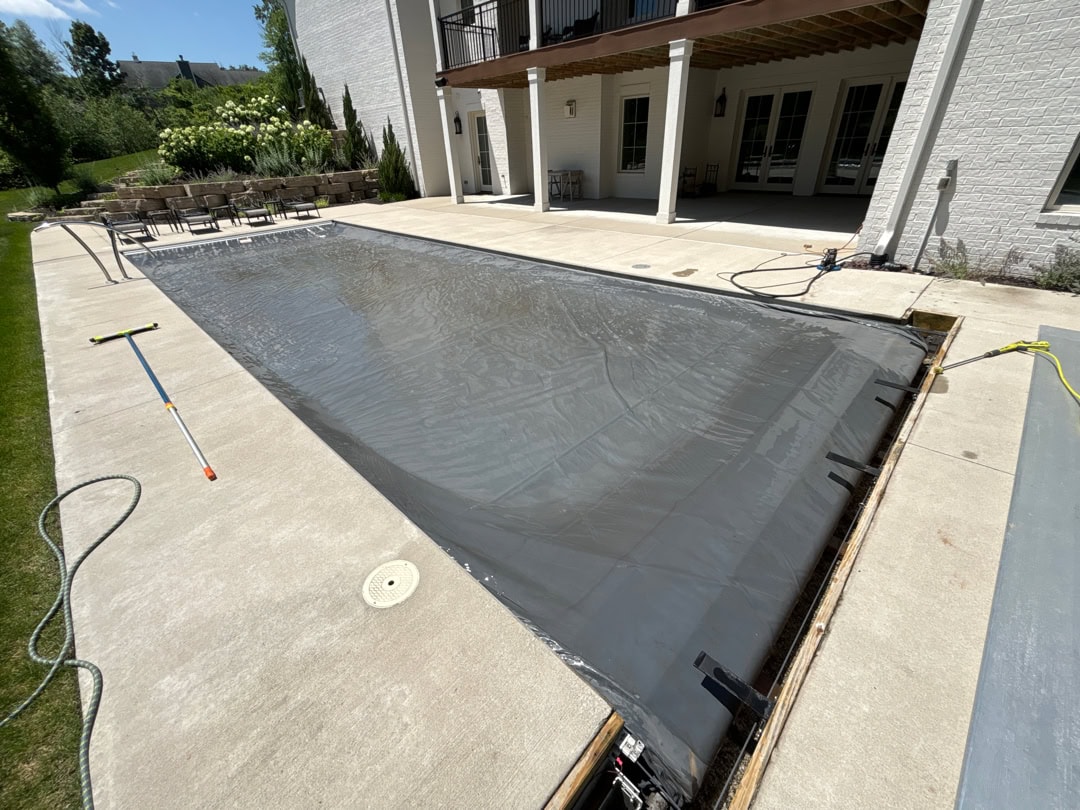 A widen shot of an inground pool with an exposed automatic cover box that is closed over the pool. The cover has recently been scrubbed with a cleaning solution and brush.