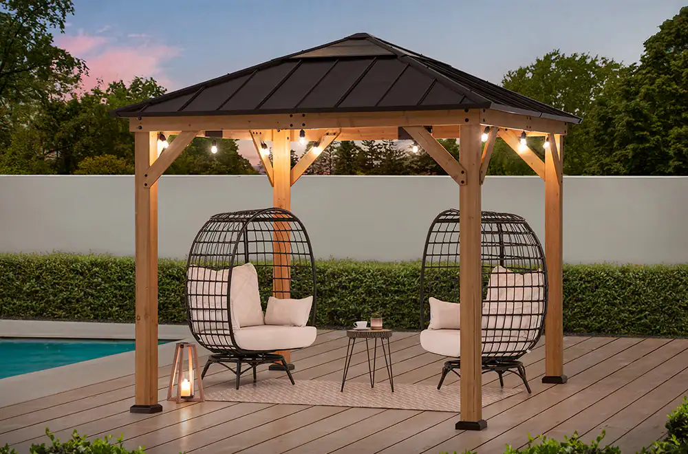 A lit gazebo next to an inground pool with two chairs under the gazebo.