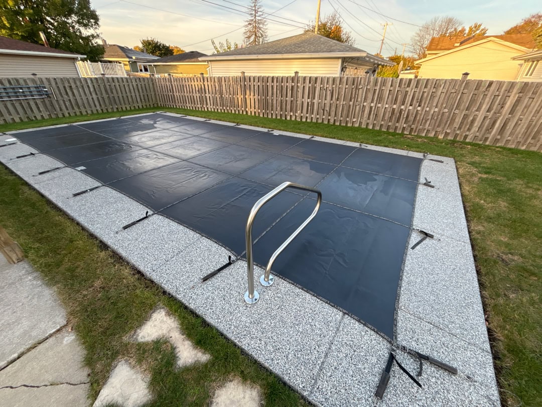 A closed inground pool with a manual winter cover covering it.