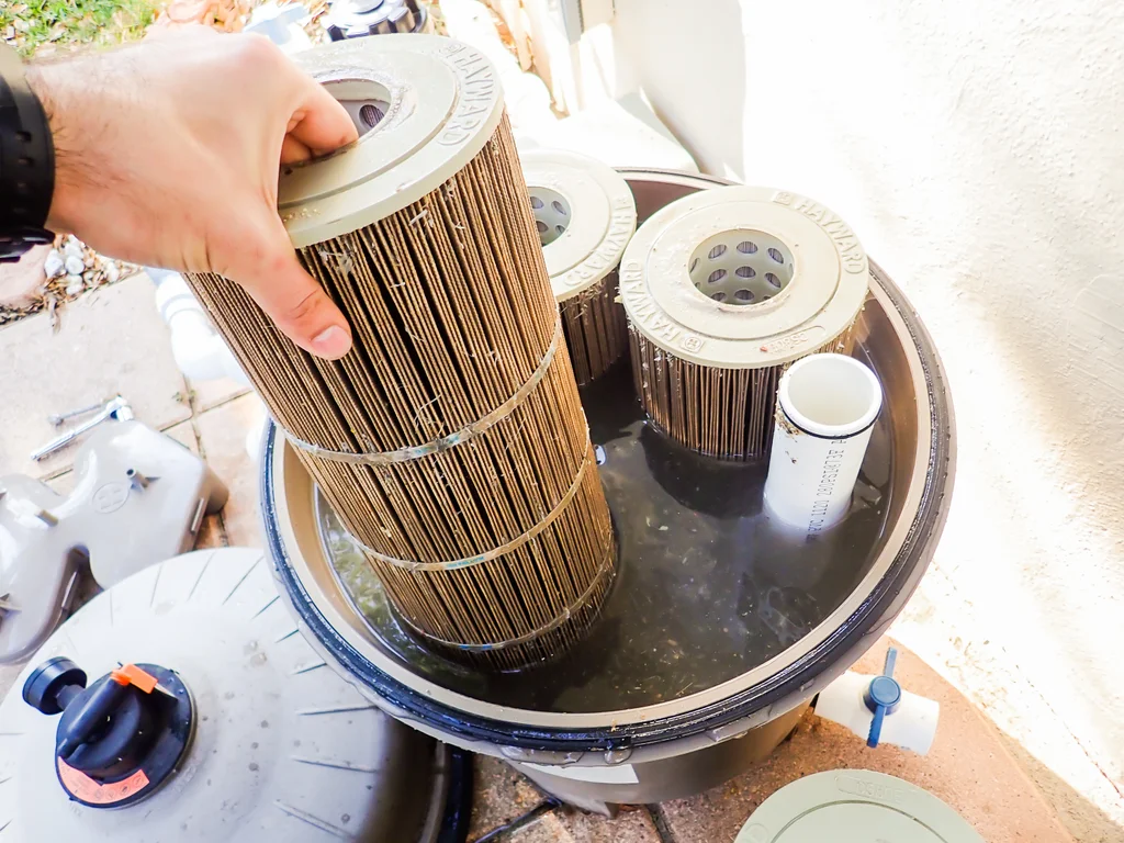 Dirty pool cartridges being removed from a cartridge filter full of black water.