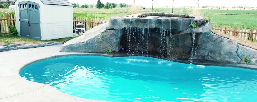 Image of the deep end of a freeform inground pool with a rock formation and spill over waterfall along the length of the pool.