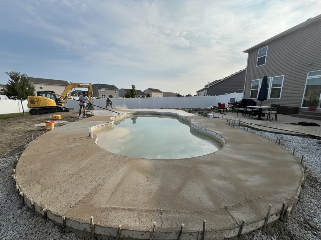 Two workers brushing concrete around an inground pool.