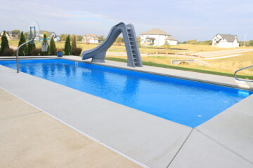A picture of a fiberglass pool with slide and basketball hoop
