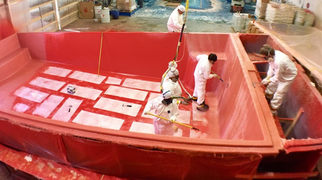 Five workers constructing a fiberglass pool in a warehouse