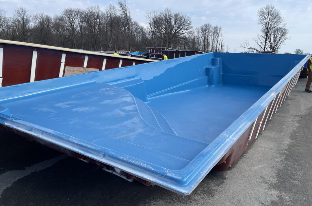 An empty fiberglass pool surrounded by other pools in a large yard.