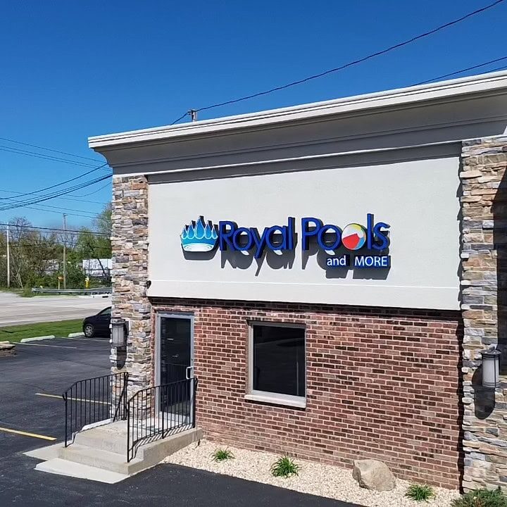 Royal Pools and More retail store face. Logo is in front of tan wall with red bricks below, with one window in the middle and a door on the left.