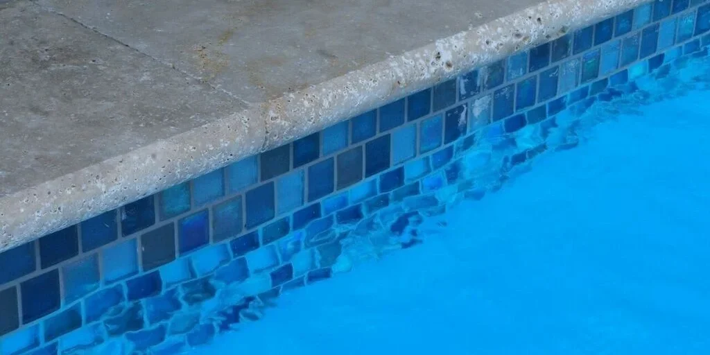 Waterline tile at the top of a fiberglass pool underneath chiseled concrete pool coping.