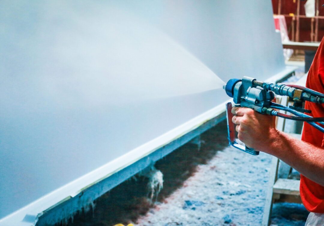 Spraying a layer of paint onto the outer shell of a fiberglass pool.