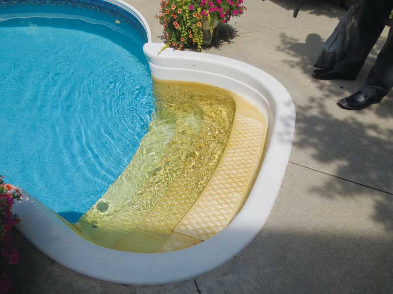 Photo of yellow-stained fiberglass pool steps in a clear vinyl liner inground pool.