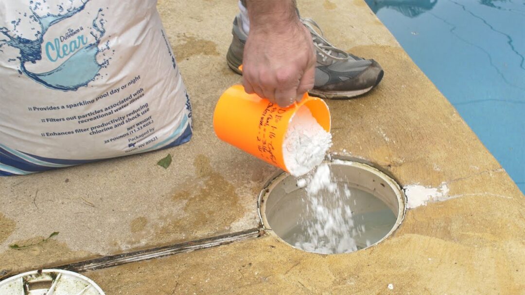 Image of a hand pouring diatomaceous earth media into a pool skimmer out of an orange scooper.