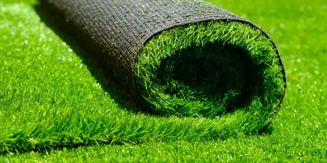 A closeup image of the side of a roll of grass turf atop a patch of grass.